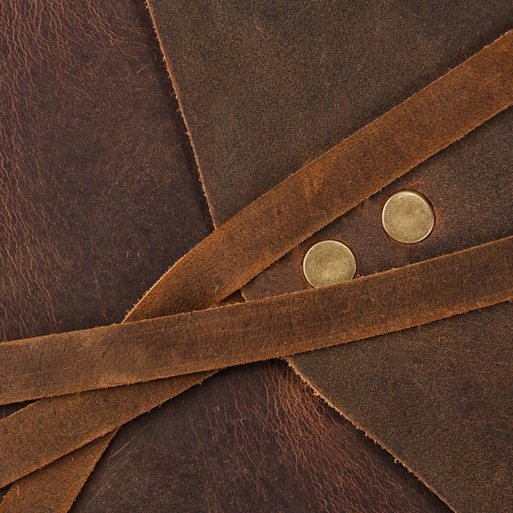 Close-up detail of the rustic full-grain leather, showing the cross-over strap and brass snap buttons.