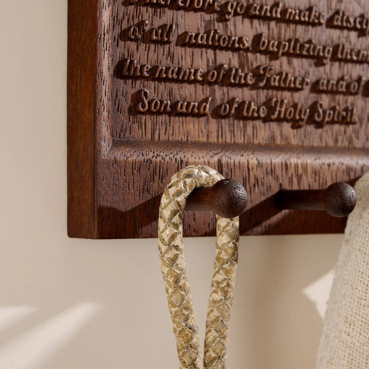 Close-up of engraved Matthew 28:19 verse and wooden hooks on Trinity wall plaque