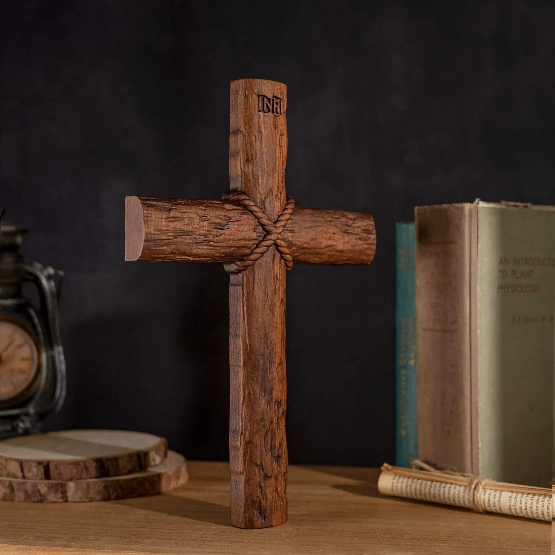 Wooden cross displayed next to a vintage lantern and wooden coasters on a dark background.