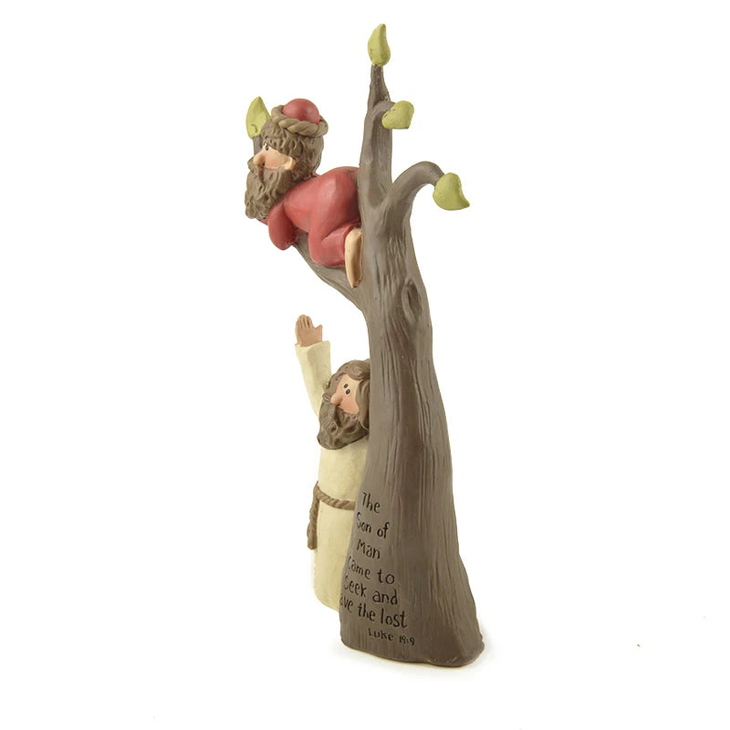 Side view of the resin sculpture depicting Zacchaeus in the sycamore tree, with a standing figure reaching up. The scripture "The Son of Man Came to Seek and Save the lost. Luke 19:10" is visible on the tree trunk.