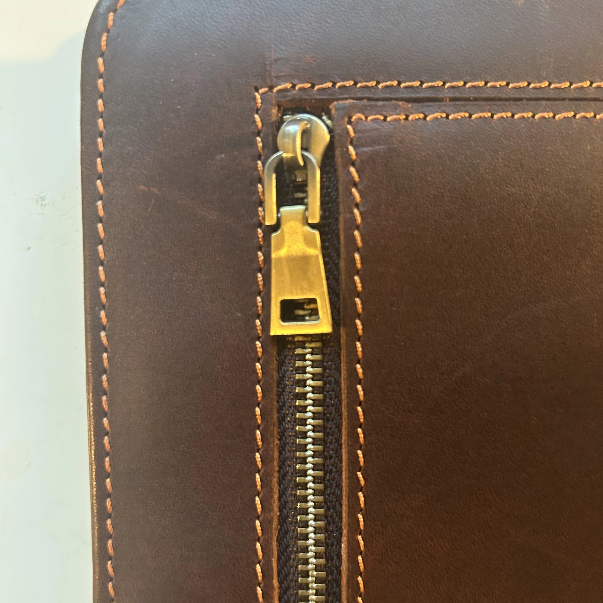 Detailed shot of the brass zipper pull on the handcrafted brown leather Bible cover.