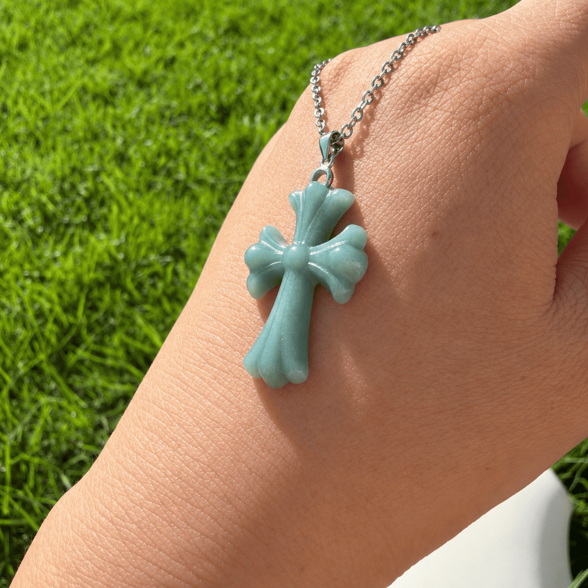 Natural Grade A blue water jadeite cross pendant shown on hand in natural sunlight