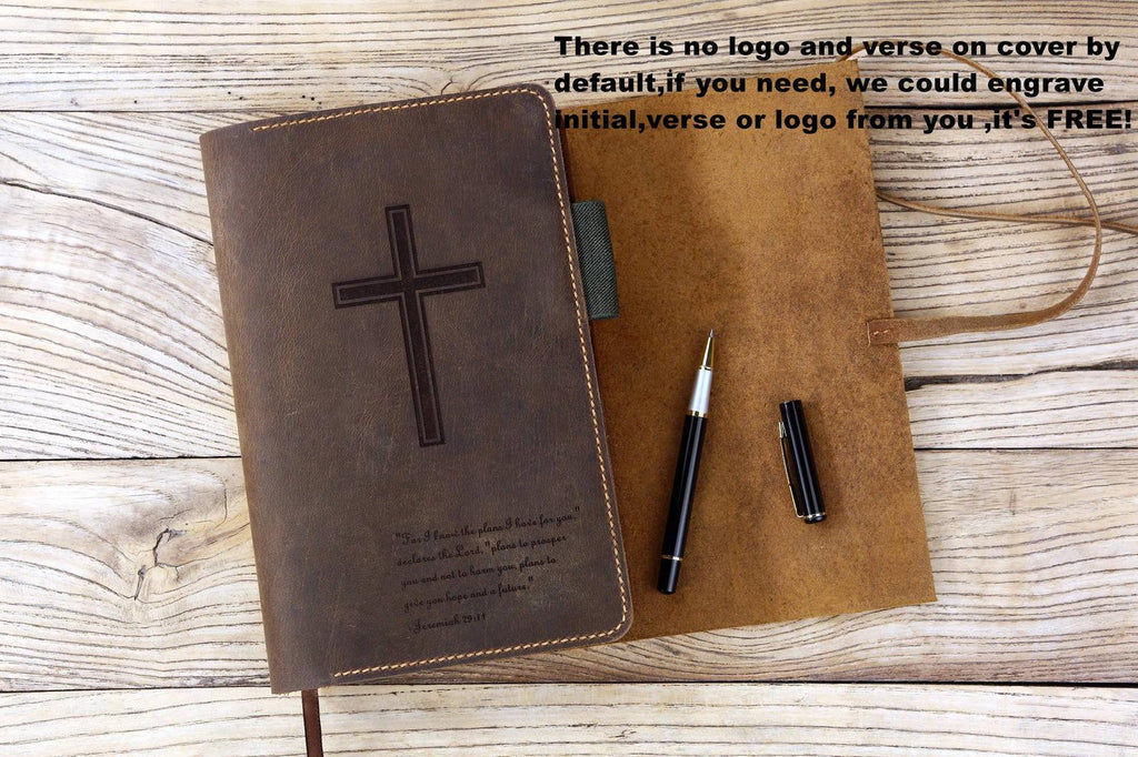 Handcrafted brown leather Bible cover with cross engraving and pen, displayed on a wooden surface.