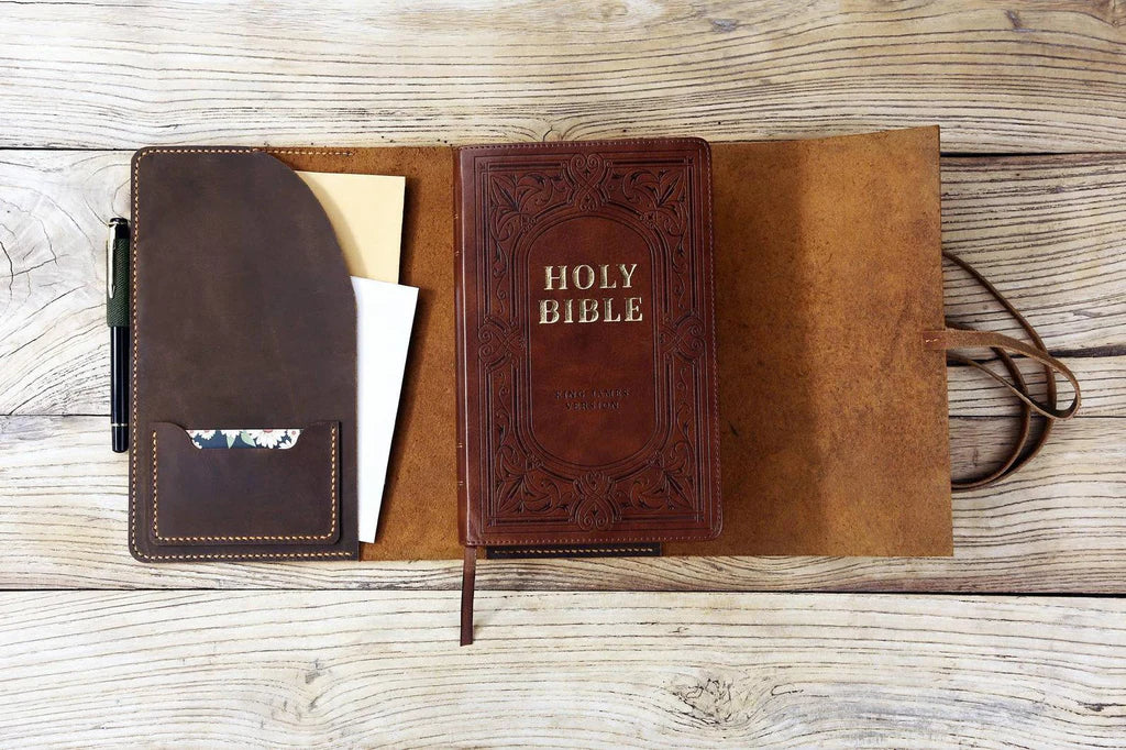 Open leather Bible cover showing interior design and Bible inside, laid flat on wooden background.