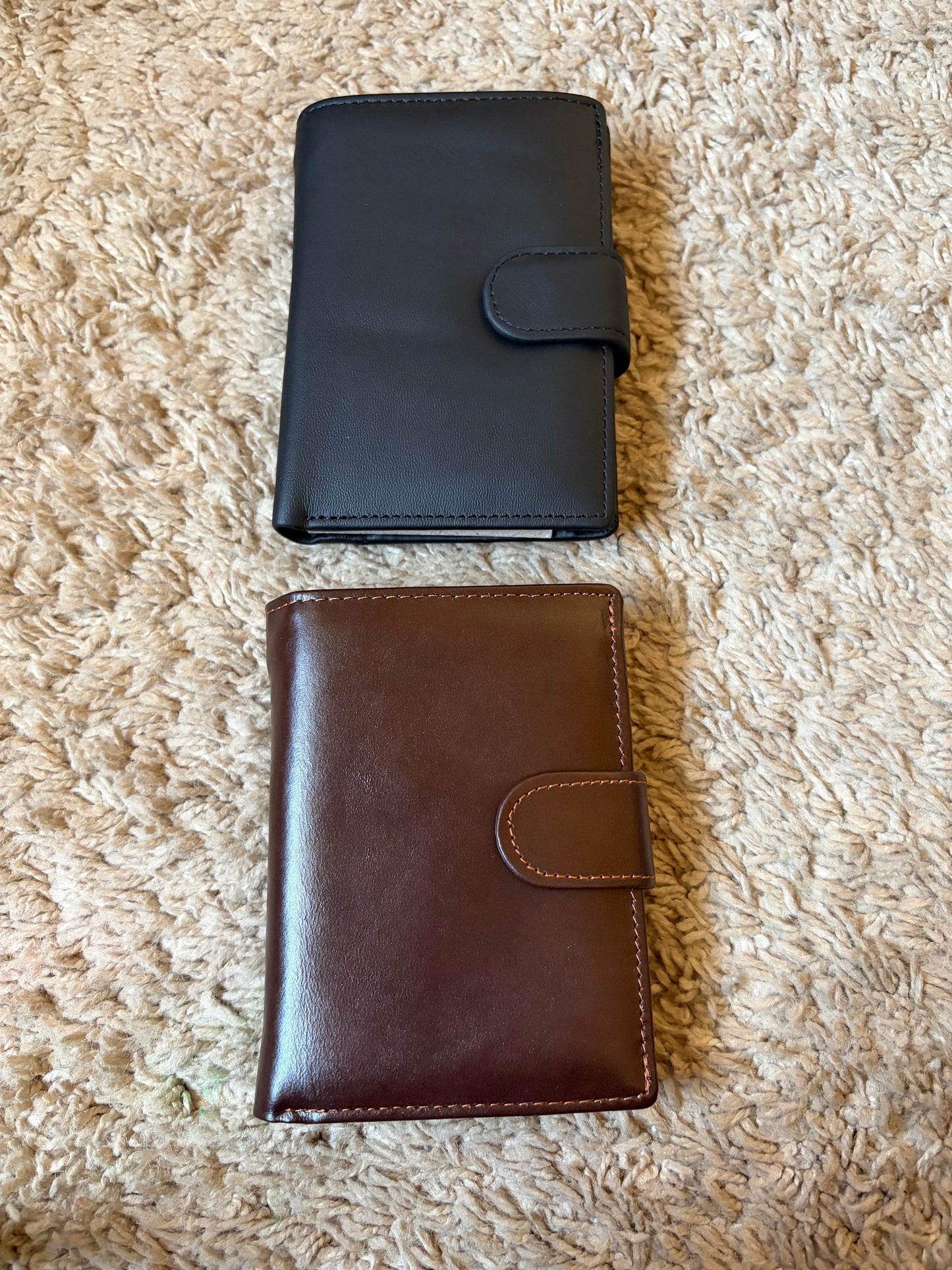 Black and brown leather wallets on a textured beige surface