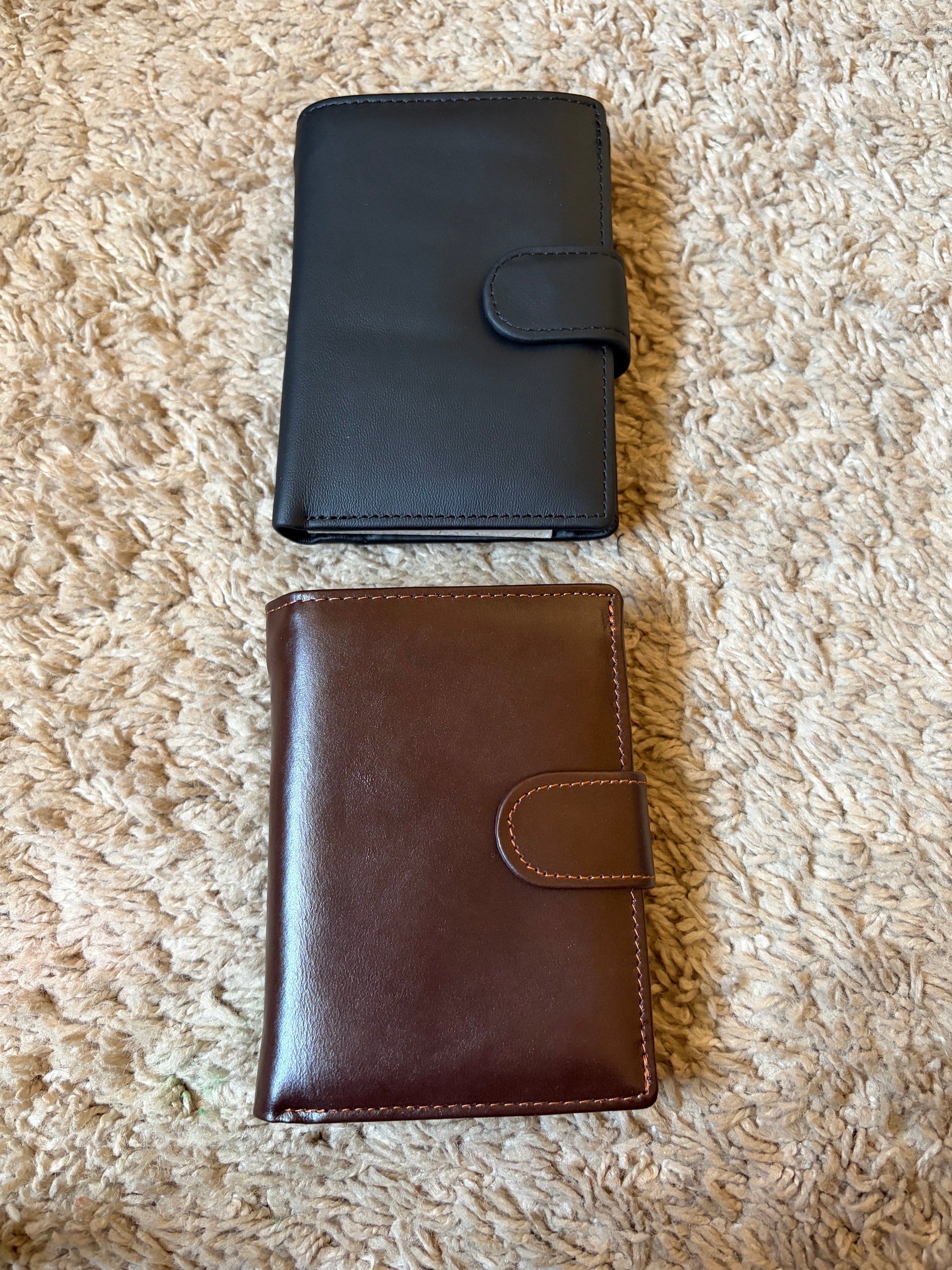 Black and brown leather wallets on a textured beige surface