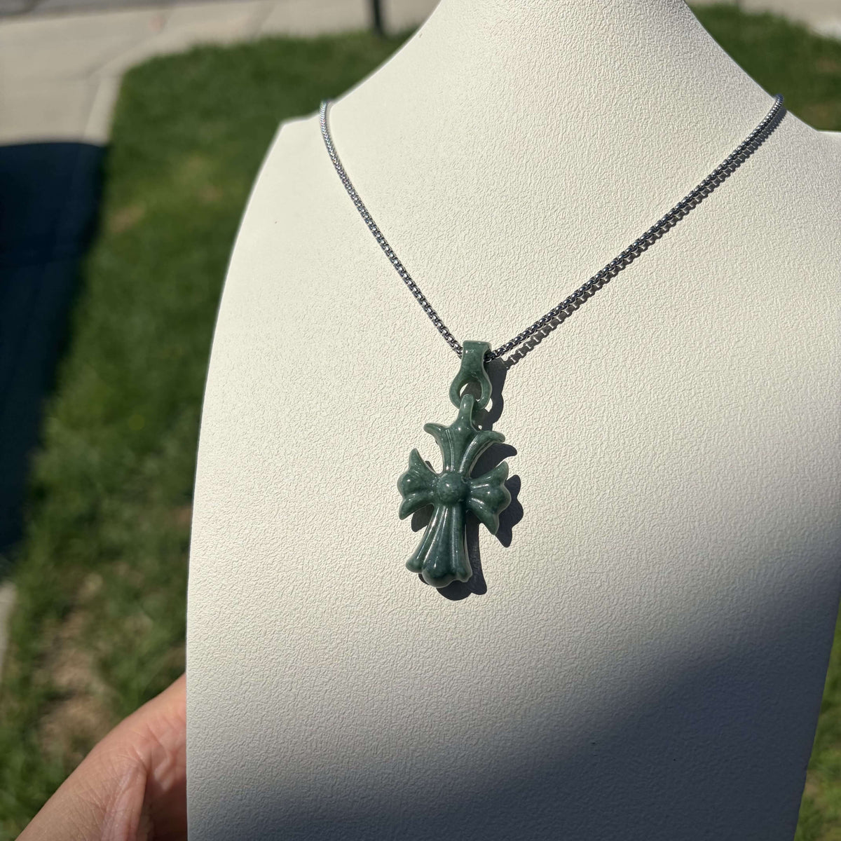 Natural Grade A bean green jadeite cross pendant displayed on a jewelry bust in natural light