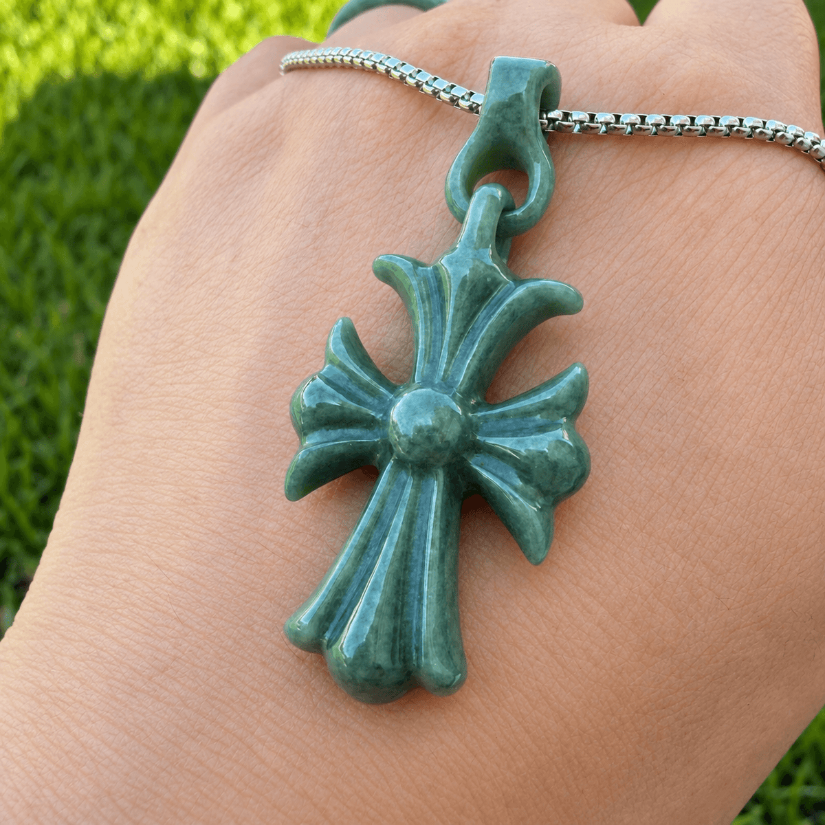 Natural Grade A bean green jadeite cross pendant shown on hand in natural light