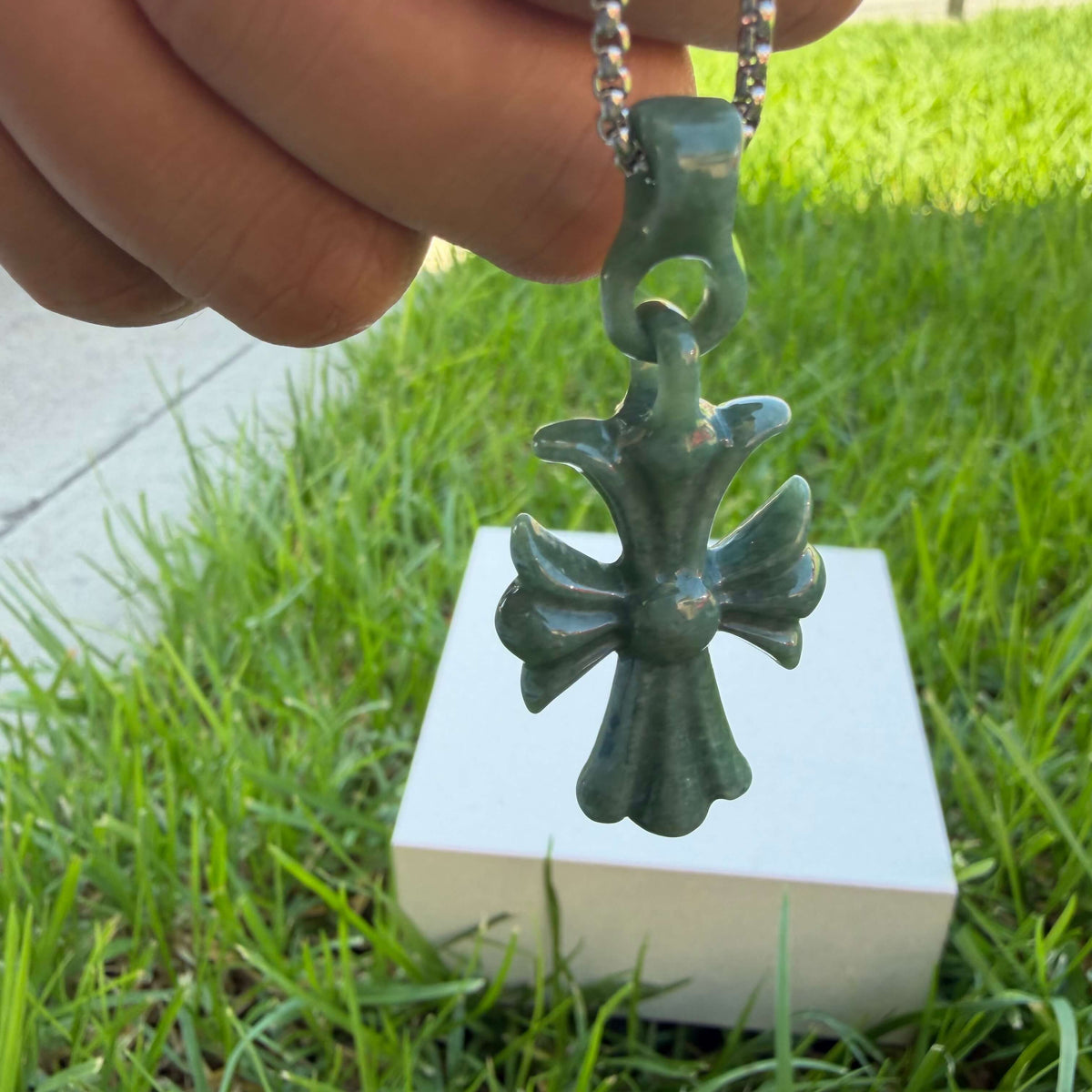 Natural Grade A bean green jadeite cross pendant held by hand outdoors in natural light