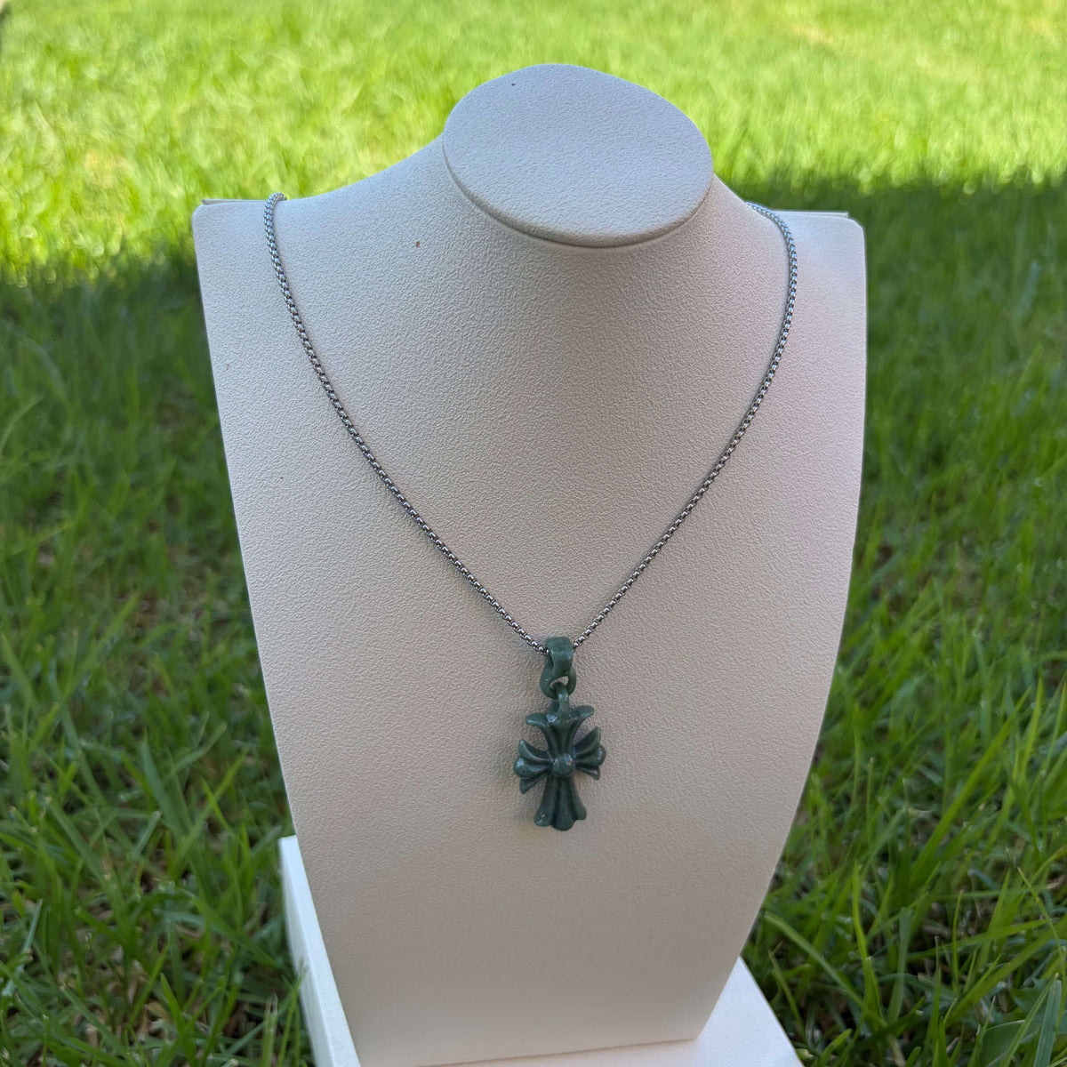 Natural Grade A bean green jadeite cross pendant displayed on a jewelry bust outdoors in natural light