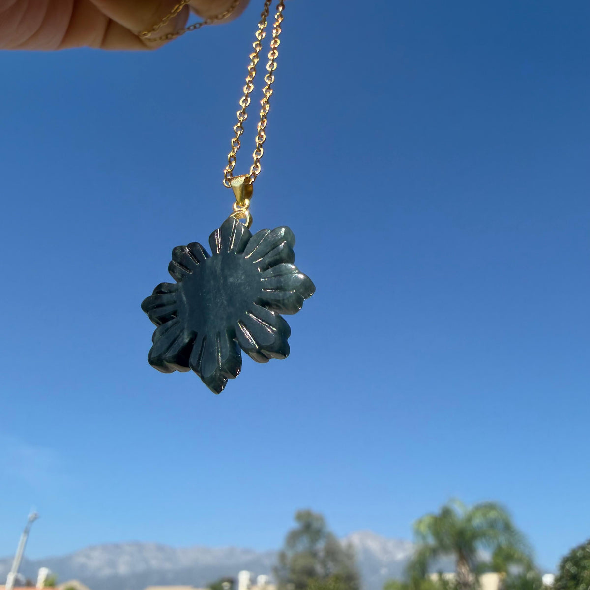 Natural untreated Wuji jadeite Filipino Sunflower pendant hanging against a blue sky