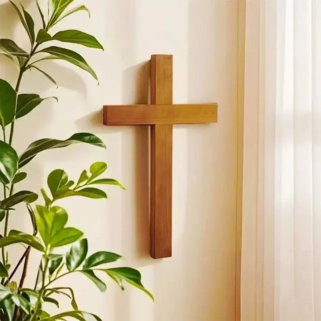 Solid cherry wood wall cross hanging on a light-colored wall with indoor plants for home decor