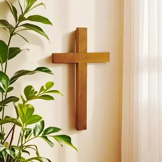 Solid cherry wood wall cross hanging on a light-colored wall with indoor plants for home decor
