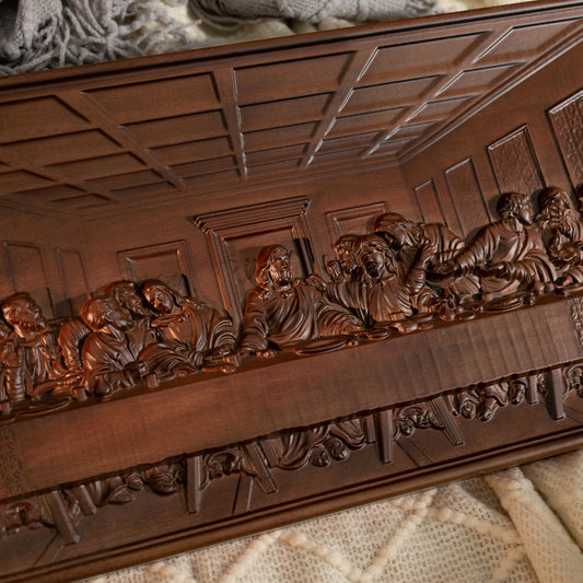 Angled view of The Last Supper wood carving from the left side, resting on a cream knitted blanket with warm light.