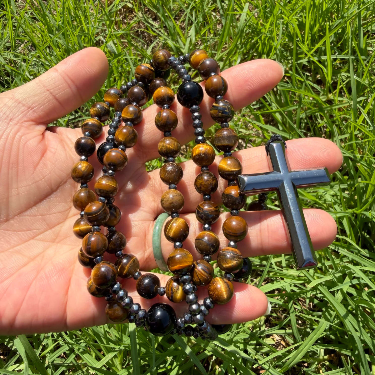 Natural Tiger's Eye rosary necklace with Hematite cross held in hand in natural light