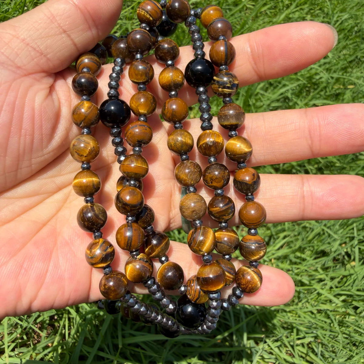 Natural Tiger's Eye rosary necklace with Hematite beads and cross held in hand in natural light